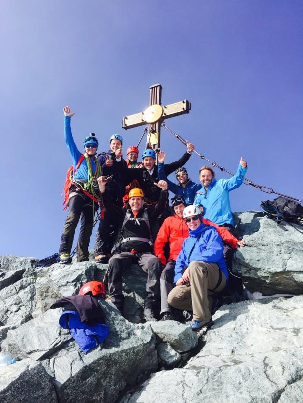 Eine Gruppe Bergsteiger posiert auf einem Gipfel mit Gipfelkreuz.