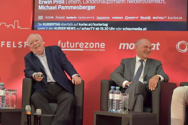 Erwin Pröll und Michael Pammesberger sitzen lächelnd auf einer Veranstaltung nebeneinander.