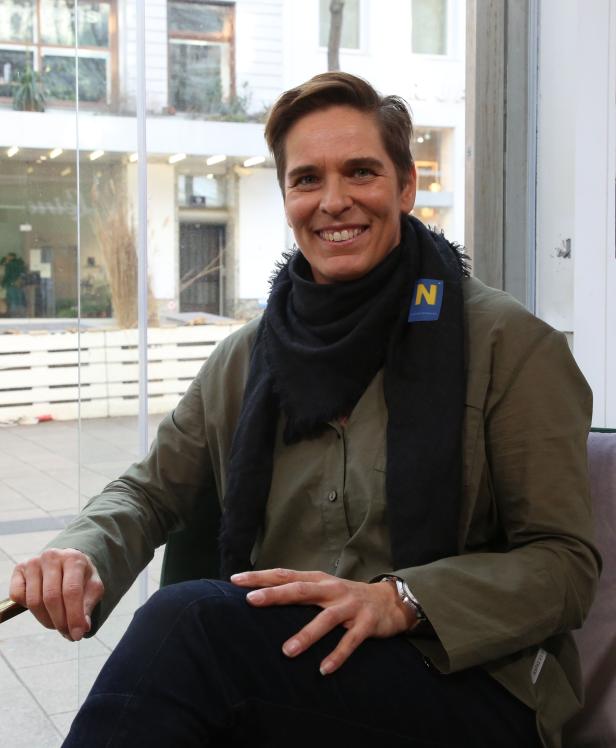 Eine Frau mit kurzem Haar sitzt in einem Sessel und lächelt.