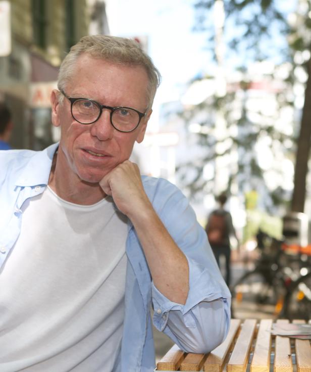 Ein Mann mit Brille sitzt an einem Tisch im Freien.