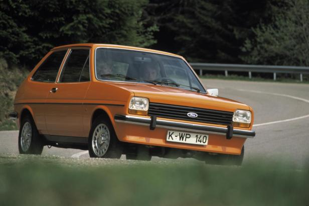 Ein orangefarbener Ford Fiesta von 1976 fährt auf einer kurvigen Straße.
