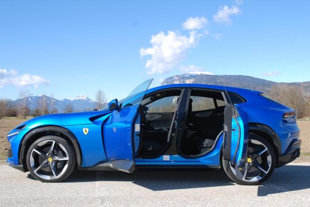 Ein blauer Ferrari Purosangue mit geöffneten Türen vor einer Bergkulisse.