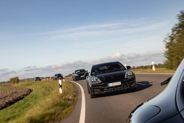 Mehrere schwarze Porsche fahren auf einer kurvenreichen Landstraße.