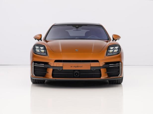 Ein orangefarbener Porsche Macan e-Hybrid von vorne auf einem weißen Hintergrund.