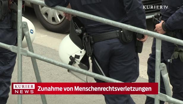 Polizisten stehen hinter einer Absperrung, Helme hängen daran.