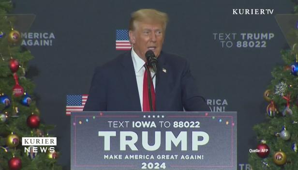 Donald Trump spricht vor einer Kulisse mit dem Slogan „Make America Great Again!“.