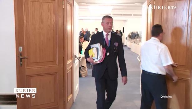 Ein Mann im Anzug trägt einen Stapel Akten durch einen Flur.