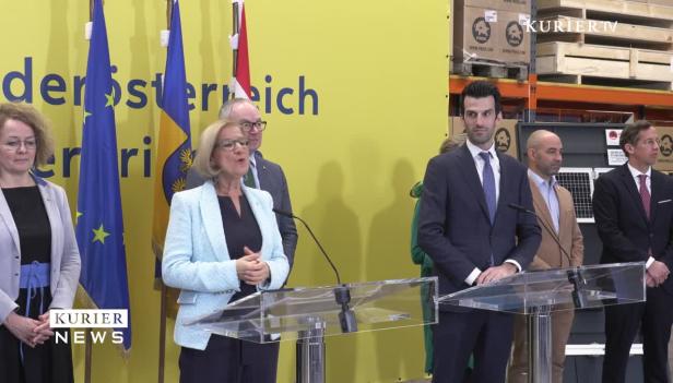 Eine Gruppe von Personen steht bei einer Pressekonferenz vor Flaggen.