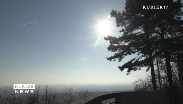 Blick von einem Hügel auf eine Stadt unter einem hellen, sonnigen Himmel.