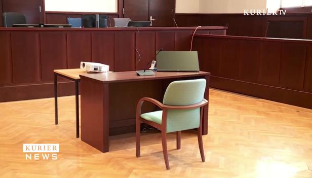 Ein leerer Gerichtssaal mit Tischen, Stühlen und technischer Ausstattung.