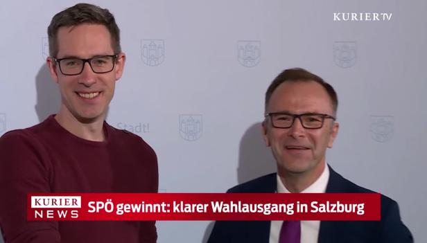 Zwei Männer stehen lächelnd vor einer Wand mit dem Salzburger Stadtwappen.