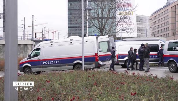 Mehrere Mannschaftswagen der Polizei stehen in Wien vor modernen Bürogebäuden.
