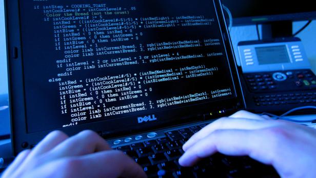 Eine Person tippt auf einem Laptop, dessen Bildschirm Code anzeigt.