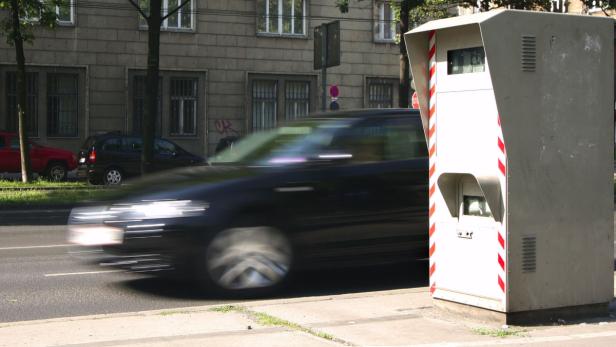 Ein Auto fährt an einem stationären Blitzer in einer Stadt vorbei.