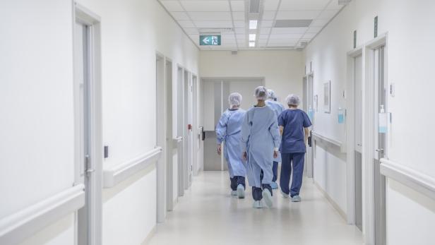 Vier medizinische Fachkräfte in Schutzkleidung gehen einen hellen Krankenhausflur entlang.