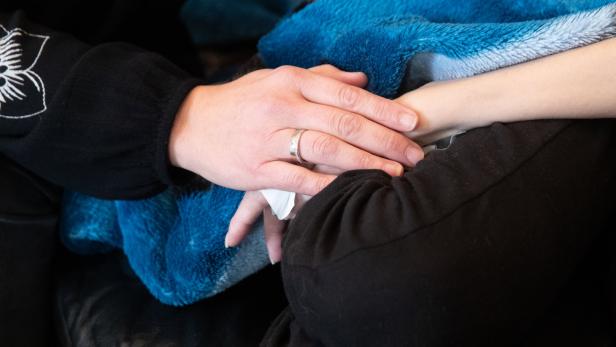 Eine Hand mit Ehering hält tröstend den Arm einer Person unter einer blauen Decke.