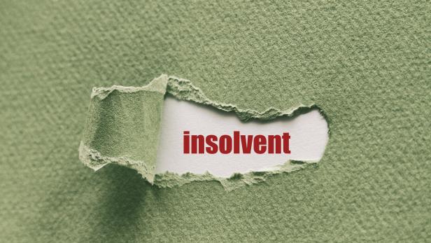 Das Wort „insolvent“ ist durch ein Loch in einem grünen Blatt Papier sichtbar.