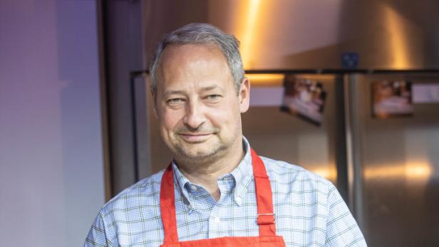 Ein Mann mit roter Schürze rührt eine helle Soße in einer Edelstahlschüssel.