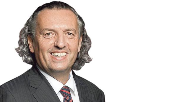 Ein lächelnder Mann mit grauem, gewelltem Haar und Anzug mit Krawatte.