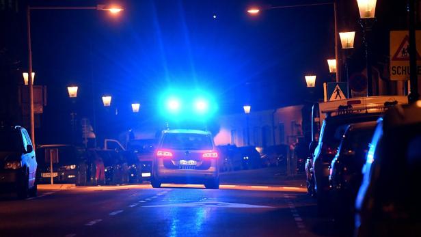 Ein Polizeiauto steht nachts mit eingeschaltetem Blaulicht auf einer Straße.