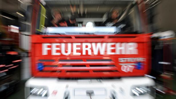 Ein rotes Feuerwehrfahrzeug mit unscharfer Frontansicht steht in einer Garage, zwei Personen sitzen vorne.