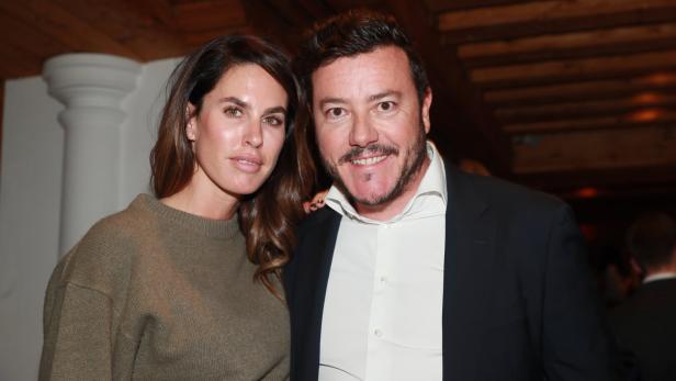 Eine Frau in einem olivgrünen Pullover und ein Mann in einem Anzug posieren für ein Foto.