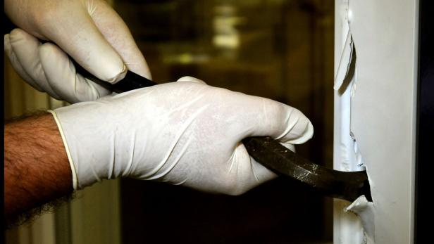 Eine Person mit Handschuhen bricht mit einem Brecheisen eine Tür auf.