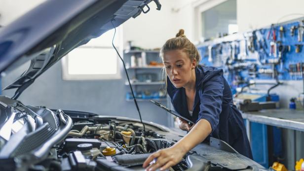 Lovely female auto mechanic, examining engine of an automobile