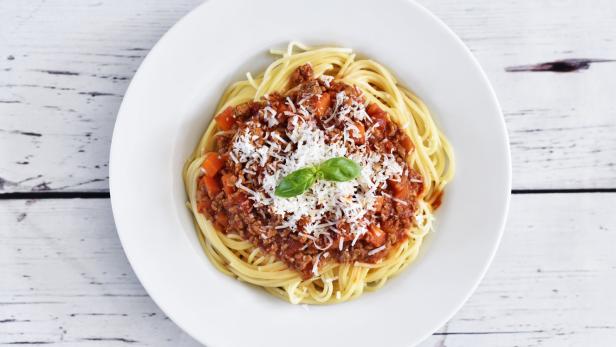 Ein Teller Spaghetti Bolognese, garniert mit Parmesan und Basilikum, auf einem Holztisch.