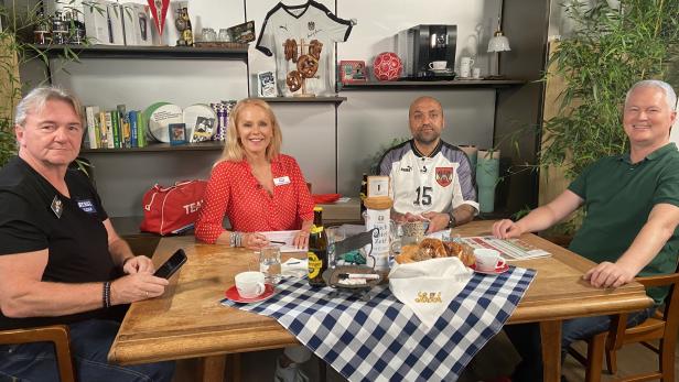 Vier Personen sitzen an einem Tisch mit österreichischen Fußballdekorationen.