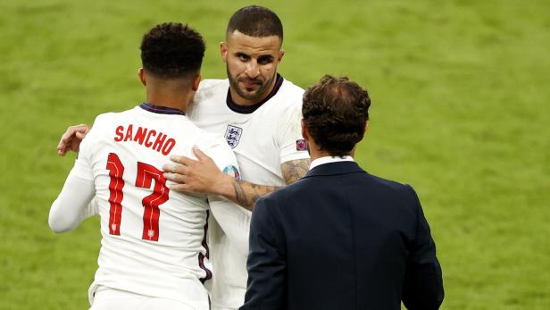 Die Fußballspieler Sancho und Walker werden von einem Trainer umarmt.