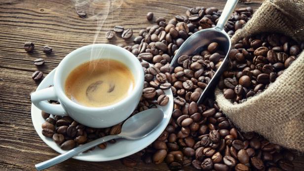Eine Tasse Kaffee mit Kaffeebohnen und einem Löffel auf einem Holztisch.