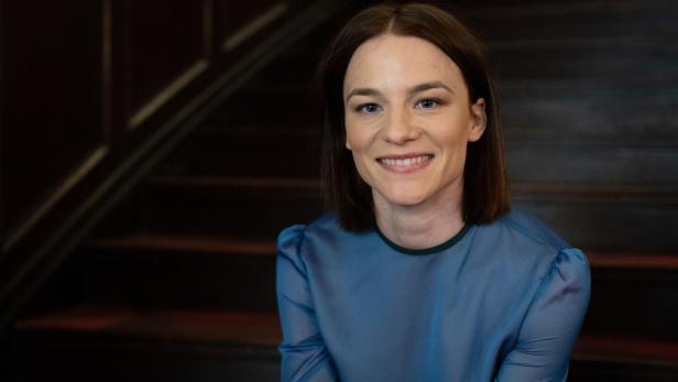 Porträt der lächelnden Schauspielerin Valerie Pachner vor einer Treppe.