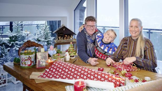 Eine Familie sitzt an einem Tisch und packt Weihnachtsgeschenke ein.