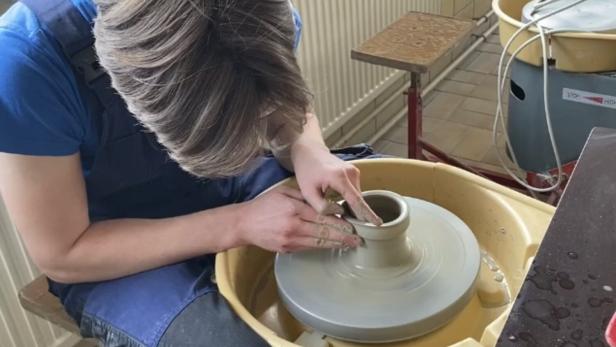 Eine Person formt mit den Händen Ton auf einer Töpferscheibe.