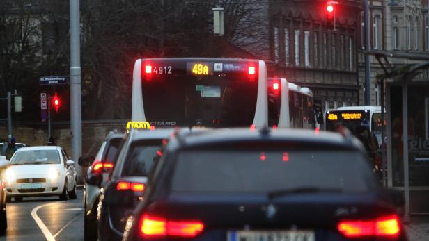 Mehrere Autos und Busse stehen bei Rot an einer Ampel in einer Stadtstraße.