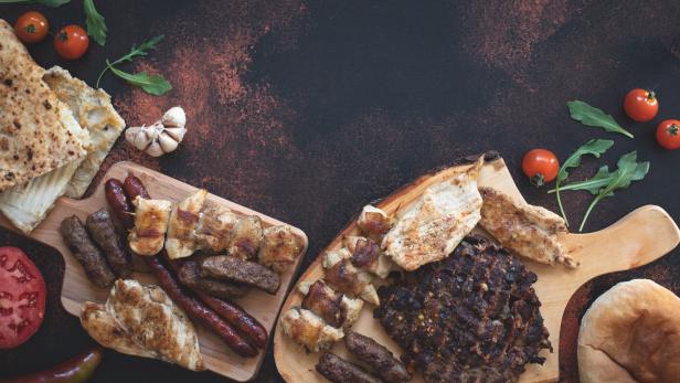 Cevapcici und gegrilltes Fleisch werden auf Holzbrettern mit Brot und Gemüse serviert.