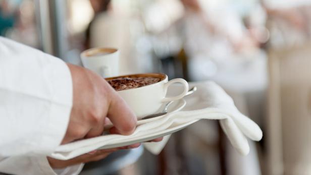Ein Kellner serviert zwei Tassen Kaffee auf einem Tablett.