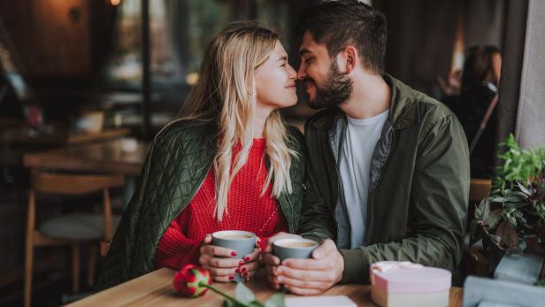 Ein verliebtes Paar sitzt in einem Café und hält Händchen über Tassen.