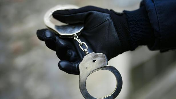 Eine Hand in einem schwarzen Lederhandschuh hält eine silberne Handschelle.