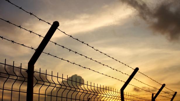 Ein Zaun mit Stacheldraht vor einem bewölkten Himmel bei Sonnenuntergang.