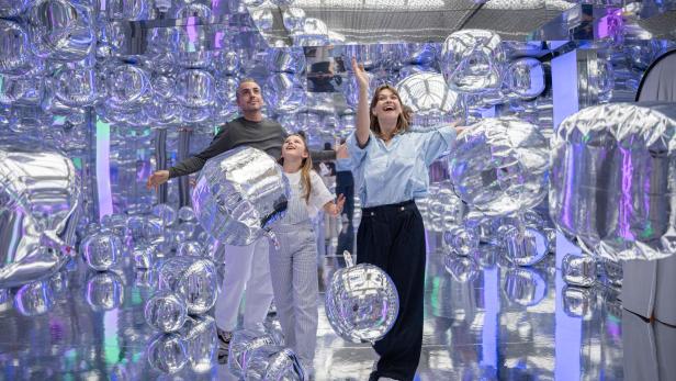 Eine Familie posiert in einer Installation mit silbernen, ballonartigen Objekten namens „Ikono“.
