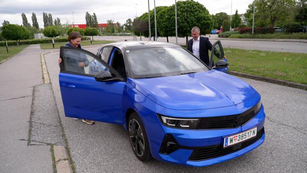 Eine Frau steigt in einen blauen Opel Astra, während ein Mann daneben steht.