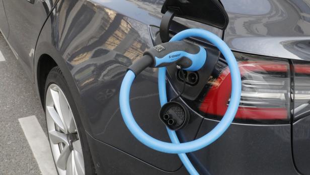 Ein graues Elektroauto wird an einer Ladestation mit einem blauen Kabel aufgeladen.