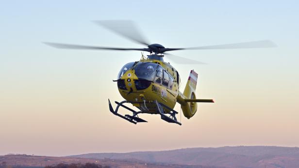 Ein gelber Rettungshubschrauber fliegt knapp über einer hügeligen Landschaft bei klarem Himmel.