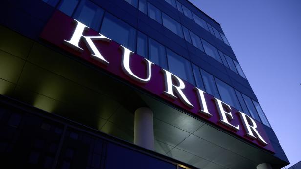 Das beleuchtete „Kurier“-Logo an einem modernen Bürogebäude bei Dämmerung.