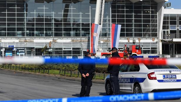 Polizisten und ein Polizeiauto vor einem beschädigten Gebäude in Serbien.