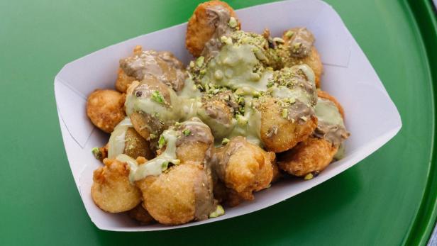 Eine Portion Fritule, überzogen mit Pistaziencreme, in einer Pappschale.