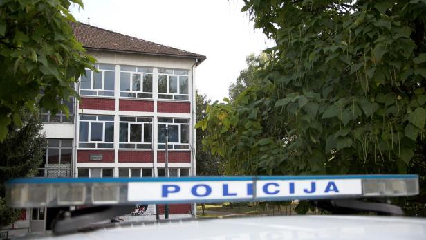 Vor einem Schulgebäude steht ein Polizeiauto mit eingeschaltetem Blaulicht.