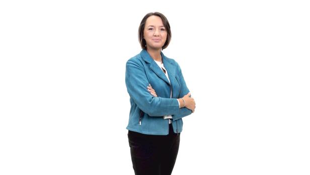 Eine Frau mit verschränkten Armen vor einem weißen Hintergrund.